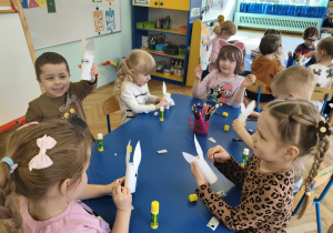 Dzieci siedzą przy stolikach, przy pomocy artykułów papierniczych wykonują króliczka wielkanocnego.