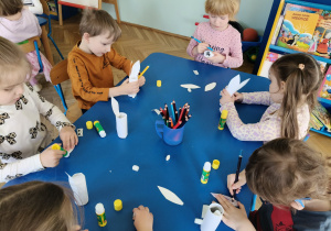 Dzieci siedzą przy stolikach, przy pomocy artykułów papierniczych wykonują króliczka wielkanocnego.