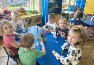 Dzieci siedzą przy stolikach, przy pomocy artykułów papierniczych wykonują króliczka wielkanocnego.