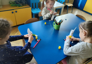 Dzieci siedzą przy stolikach, przy pomocy artykułów papierniczych wykonują króliczka wielkanocnego.