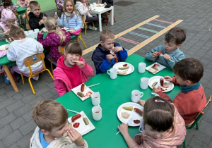 dzieci siedzą przy stolikach na tarasie spożywając posiłek