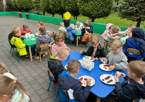 dzieci siedzą przy stolikach na tarasie spożywając posiłek