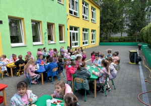 dzieci siedzą przy stolikach na tarasie spożywając posiłek