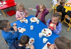 dzieci siedzą przy stolikach na tarasie spożywając posiłek
