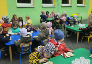 dzieci siedzą przy stolikach na tarasie spożywając posiłek