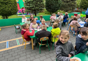 dzieci siedzą przy stolikach na tarasie spożywając posiłek