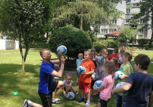 Dzieci patrzą na trenera, który pokazuje jak kręcić piłkę na palcu
