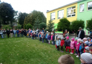 Dzieci i rodzice stoją w wielkim kole w przedszkolnym ogrodzie