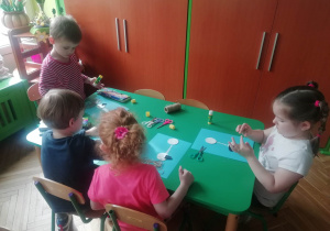 Dzieci siedzą przy stolikach, przyklejają elementy bociana do kartki.