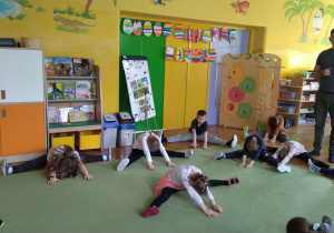 Dzieci siedzą na dywanie i wykonują szpagat