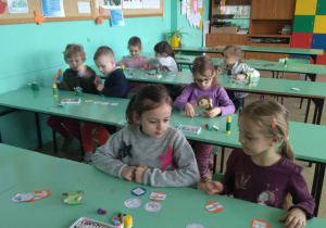 Dzieci siedzą w szkolnych ławkach i słuchają instrukcji nauczyciela