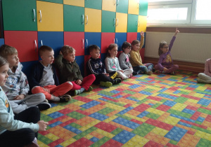 Dzieci siedzą na kolorowym dywanie, zgadują kolory w języku angielskim