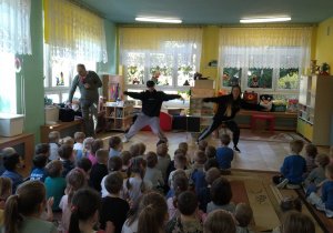 2 tancerzy prezentuje swoje umiejętności taneczne. Dzieci siedzą na dywanie i obserwują prezentację.