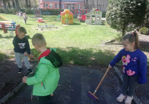 Dzieci zamiatają chodnik przedszkolny.