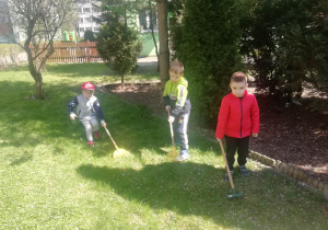 Dzieci garbią trawnik w ogrodzie przedszkolny.