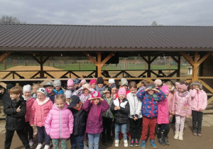 duża grupa dzieci stoi na tle zagrody dla Alpak