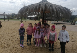 Grupa dziewczynek stoi na plaży pod drewnianą palmą