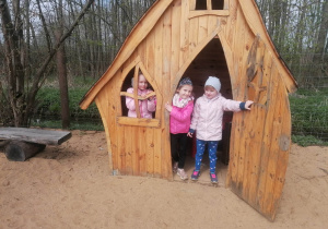 Trzy dziewczynki znajdują się w drewnianym domku na placu zabaw