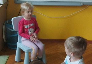Dziewczynka siedzi na krzesełku przed tablicą multimedialną i opowiada.