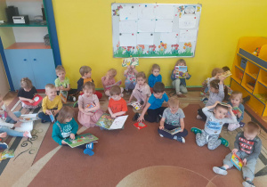 Dzieci siedzą na dywanie i pokazują książki