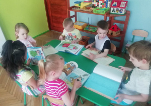 Dzieci siedzą przy stoliku i oglądają książki