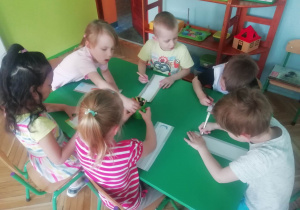 Dzieci siedzą przy stoliku i ozdabiają zakładki do książki