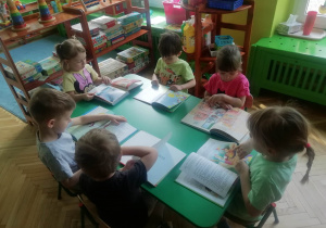 Dzieci siedzą przy stoliku i oglądają książki