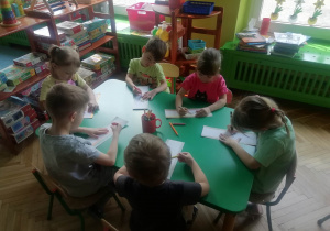 Dzieci siedzą przy stoliku i ozdabiają zakładki do książki