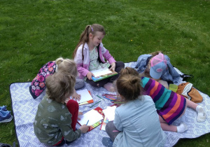Dzieci siedzą na kocu w ogrodzie, Oglądają książki, wykonują rysunki