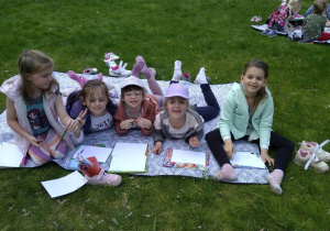 Dzieci siedzą i leżą na kocach w ogrodzie, Oglądają książki, wykonują rysunki