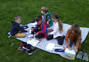 Dzieci siedzą na kocu w ogrodzie, Oglądają książki, wykonują rysunki