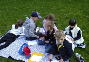 Dzieci siedzą, leżą na kocu w ogrodzie, Oglądają książki, wykonują rysunki