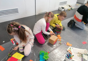 Troje dzieci wykonuje prace plastyczną oklejając pudełka