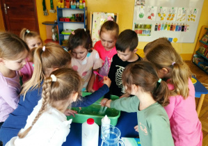 Dzieci z grupy niebieskiej robią własnoręcznie slime. Wlewają do miski klej, płyn do soczewek, sodę oczyszczona i barwnik spożywczy.