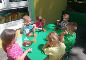dzieci siedzą przy stoliku i konsumują obiad na tarasie przedszkolnym