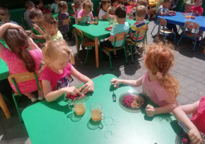 dzieci siedzą przy stoliku i konsumują obiad na tarasie przedszkolnym
