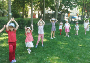 dzieci z grupy żółtej i srebrnej uczestniczą w zajęciach jogi w ogrodzie, wykonują pozycję drzewa