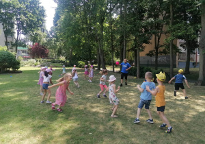 Grupa dzieci biega po ogrodzie, trener biega z różową piłką