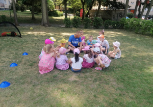 Dzieci wraz z trenerem siedzą na trawie i omawiają zasady zabawy