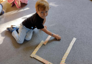 Chłopiec układa domino na dywanie