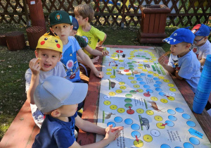 chłopcy siedzą przy stole w ogrodzie i graja w grę planszową