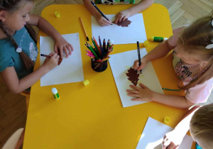 Dzieci przy stolikach naklejają liście