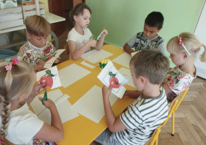 Dzieci siedząc przy stoliku wycinają puzzle z ilustracją jabłka.