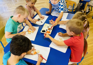 Dzieci malują farbami wiewiórkę z drewna