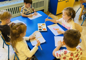 Dzieci malują farbami wiewiórkę z drewna