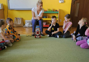 Dzieci słuchają Pani Kasi siedząc na dywanie.