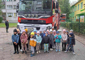 Grupa czerwona pozuje do zdjęcia grupowego, w tle wóz strażacki