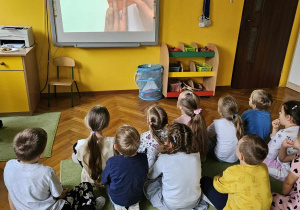 Dzieci siedzą na dywanie oglądając film instruktarzowy