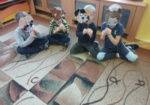 Dzieci siedzą na dywanie prezentując swoje prace