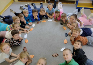 Dzieci z grupy pomarańczowej leżą na dywanie i pozują do zdjęcia grupowego